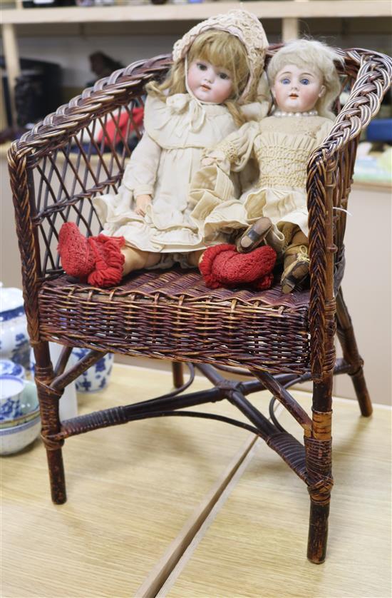 Two bisque headed 19th century dolls on a wicker chair